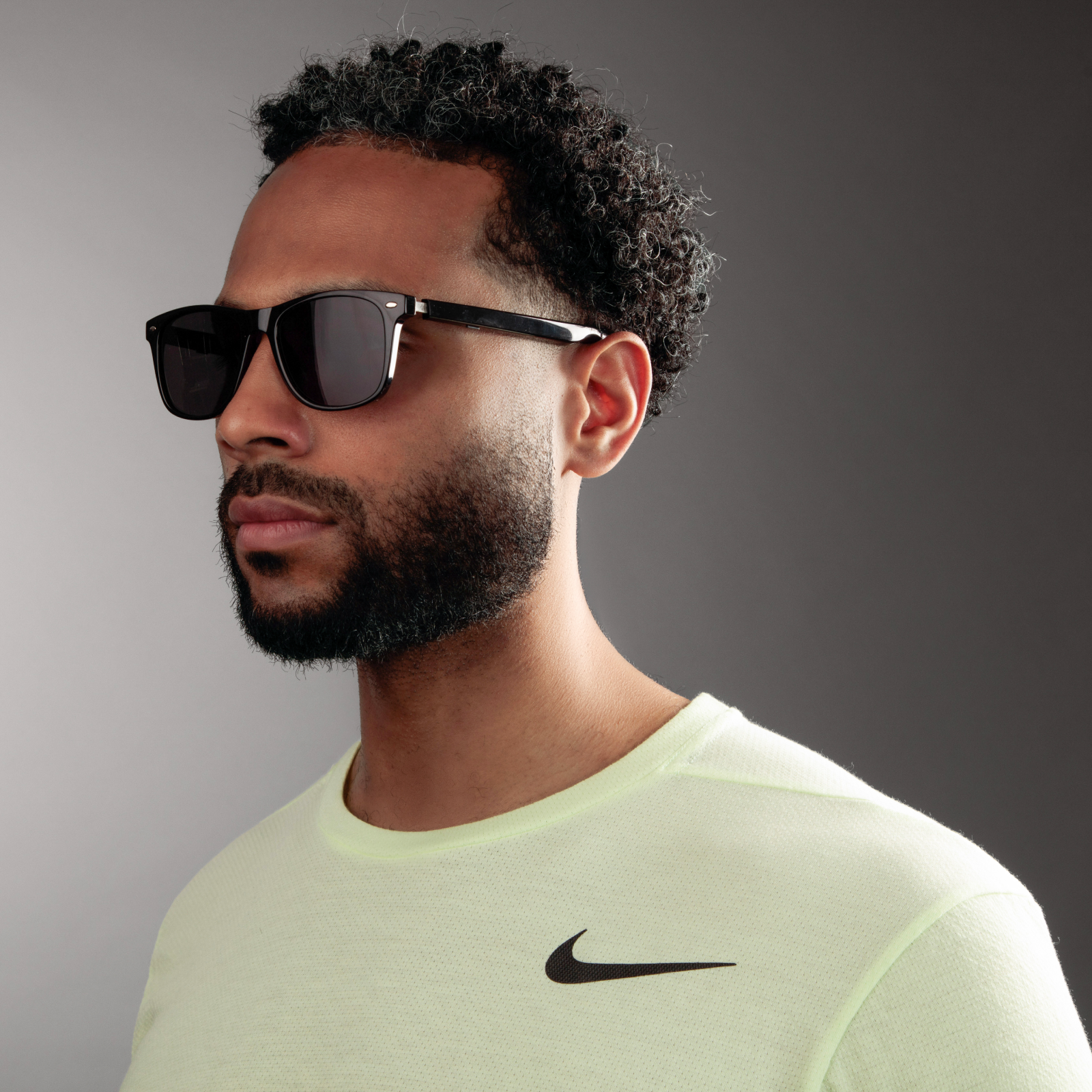 Man wearing sunglasses and a light green Nike shirt against a gray background