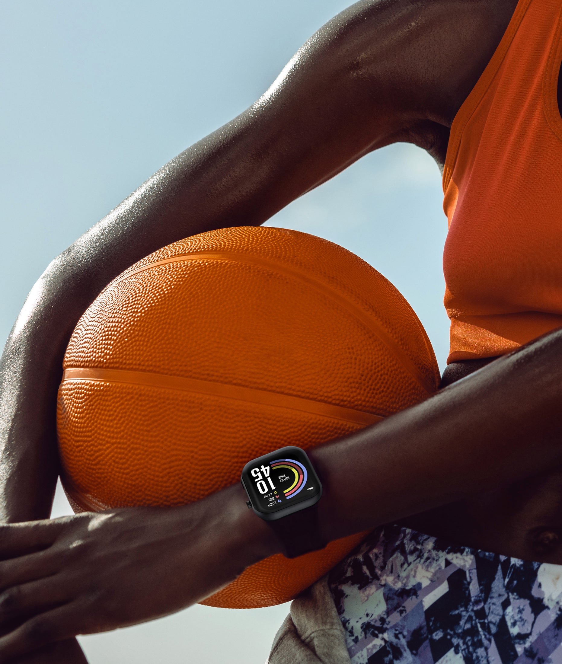 Person holding a basketball with a air 5 pro smartwatch on the wrist, wearing an orange sleeveless shirt.